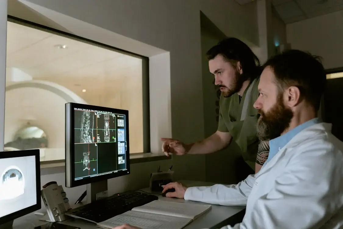 The Use of Business Intelligence in Healthcare and Why It Matters Two medical professionals, one in a lab coat and one in green scrubs, studying medical imaging on a computer screen in a darkened radiology suite.